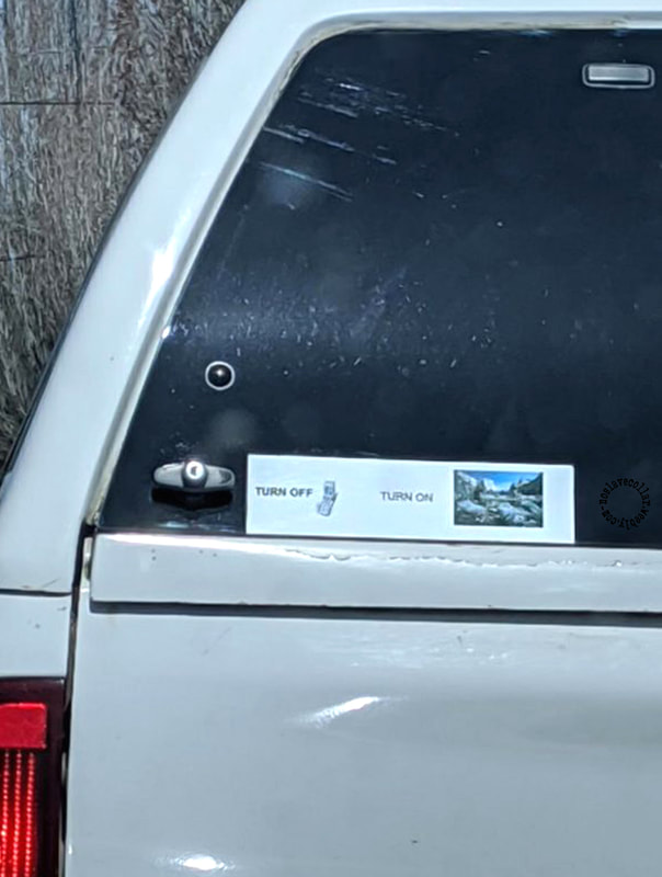 At the back of a car, a sticker reads: 'Turn off (your phone), Turn on (the scenery)'